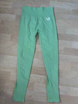 Gröna sömlösa leggings - Snygga ljusgröna sömlösa leggings med hög midja och ribbade detaljer. Stretchigt material som sitter skönt och formar sig efter kroppen. Liten vit logga med hjärta på höften. Perfekta för träning eller chill.