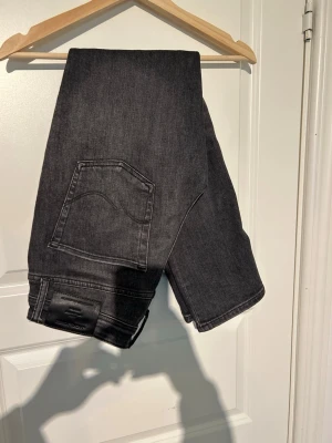 Svarta raka jeans från Jack and Jones  - Säljer ett par svarta jeans med rak passform och klassiska bakfickor. Jeansen har en stilren look och är tillverkade i denim. Perfekta för dig som gillar en enkel och clean stil.