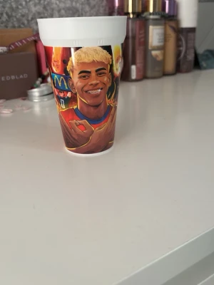 Lamine yamal kopp - Cool plastmugg med färgglatt tryck av en fotbollsspelare i röd och blå matchtröja, eldflammor och sportiga detaljer. Perfekt för dig som gillar fotboll och vill ha en unik mugg till drycken. Muggen är vit upptill och har ett livfullt motiv runt om. Aldrig använd Eller tvättad, endast uttagen ur förpackning.