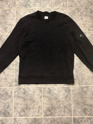 Cp company sweatshirt - En stilren svart sweatshirt från cp company Tröjan har en patchdetalj på vänster ärm perfekt för en avslappnad look
