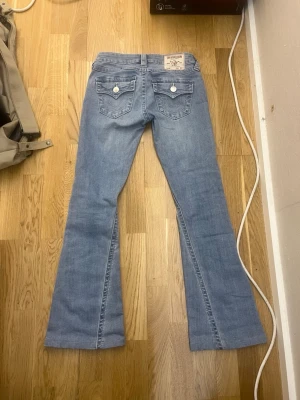 Ljusblå true religion bootcut jeans med fickdetaljer - Säljer ett par true religion ljusblå bootcut jeans. Dom är upp sydda till min längd när jag va ca 160-161cm lång så dom är inte original längden, byxorna är ca 87,5cm från midjan o ner. Jag tycker att dom har storpass form runt midjan för nån som har xs-xxs på andra jeans.