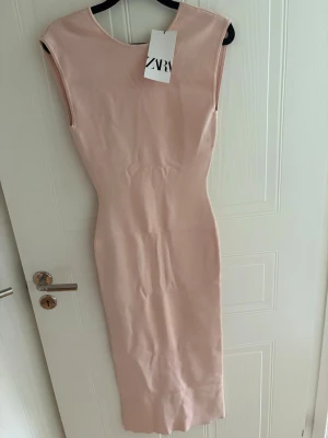 Ljusrosa långklänning med öppen rygg - Säljer en elegant ljusrosa långklänning från ZARA med figurnära passform. Klänningen har en djup öppen rygg med tunna korsade band och är ärmlös. Perfekt för sommarens alla tillfällen.