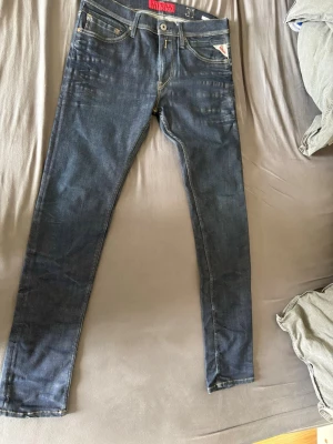 Replay Jeans  - Säljer ett par mörkblå slim fit jeans med klassisk femficksdesign och kontrastsömmar. Jeansen har en snygg tvätt och smal passform som sitter tajt längs benen. Perfekta för dig som gillar en modern och stilren look.