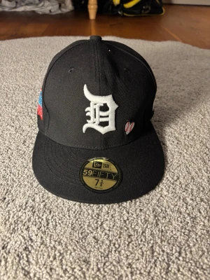 Svart New Era 59FIFTY Detroit keps - Snygg svart fitted keps från New Era 59FIFTY med Detroit D-broderi framtill och små broderade detaljer på sidorna. Baksidan har texten 'LOVE & HUSTLE GAME' och MLB-logga. Klassisk rak skärm och hög krona. Perfekt för dig som gillar streetwear och sportig stil.