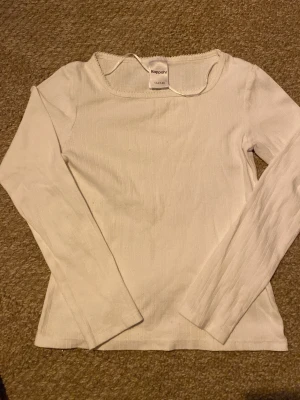 Vit långärmad topp från Kappahl - En enkel och stilren vit långärmad topp från Kappahl. Toppen har en rund halsringning och är tillverkad i ett mjukt, ribbat material som ger en skön passform. Perfekt att matcha med jeans eller kjol för en clean look.