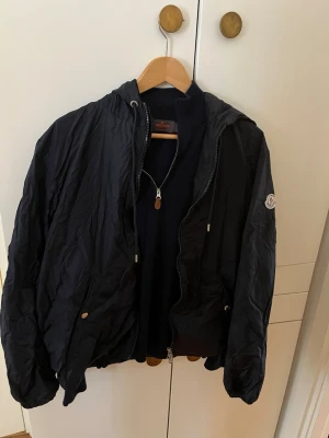 Svart vindjacka med huva - Snygg marinblå vindjacka från moncler den har den klassiska luvan och detaljerna på framsidan. Passar perfekt in för hösten