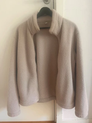 Beige teddyjacka med dragkedja - Mysig beige teddyjacka ifrån uniqlo med hög krage och hel dragkedja framtill. Jackan har en avslappnad passform och är tillverkad i mjukt, fluffigt teddy-material som håller dig varm. Perfekt för lager-på-lager och chill dagar.