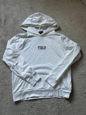 Vit hoodie från Polo Ralph Lauren - Snygg vit hoodie från Polo Ralph Lauren med broderad logga på bröstet. Klassisk modell med huva och känguruficka framtill. Tillverkad i mjukt bomullsmaterial som känns skönt mot huden. Perfekt för en clean och stilren look.