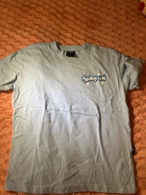 Ljusblå Hoodrich t-shirt med tryck - Säljer en ljusblå t-shirt från Hoodrich med flera coola tryck i graffiti-stil på både bröstet och ryggen. T-shirten är kortärmad och har en relaxed passform. Perfekt för dig som gillar streetwear och vill sticka ut lite extra.