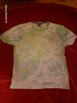 Tie-dye t-shirt från Tommy Hilfiger - Säljer en tie-dye t-shirt från Tommy Hilfiger i storlek XXL. T-shirten är i ljusa pastellfärger med gröna och blå toner och har en liten logga på bröstet. Tillverkad i ekologisk bomull för extra skön känsla. Perfekt för dig som gillar en avslappnad och trendig stil.
