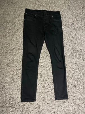Svarta Jeans från Nudie  - Snygga svarta skinny jeans med klassisk femficksdesign och smal passform. Jeansen har bälteshällor och subtila sömdetaljer på bakfickorna. Perfekta för en stilren och modern look. W32 L32