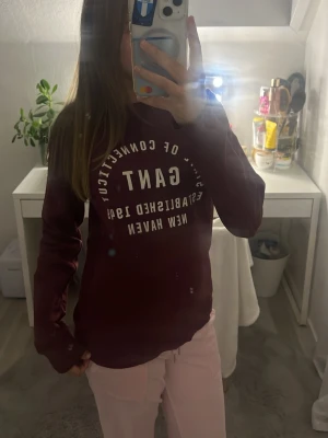 Vinröd tröja från GANT - Säljer en vinröd tröja från GANT med vit text och logga på bröstet. Tröjan har rund halsringning, ribbade muddar och är tillverkad i mjukt bomullsmaterial. Perfekt för en avslappnad och stilren look. Storlek 158/164 men är som xs/s