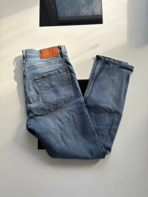 Ljusblå slitna jeans med hål - Säljer ett par ljusblå jeans med skinny fit och flera slitningar och hål på framsidan. Jeansen har klassisk femficksdesign, bruna sömmar och en läderpatch bak i midjan. Perfekta för en avslappnad och trendig streetstil.