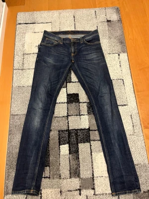 Mörkblå tight long John nudies  - Snygga mörkblå slim fit jeans med klassisk femficksdesign och lätt slitna detaljer. Jeansen har normal midja och smal passform hela vägen ner. Perfekta till en avslappnad stil och passar till det mesta.
