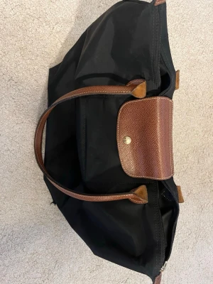 Longchamp Väska - Säljer denna då jag köpt en ny. Den har används i många år och har därför hål i alla fyra kanter på undersidan, inte stora endast hål man rymmer pekfingret i. Dragkedjan på väskan fungerar inte och därför går den inte att stänga. Väskan har också lite fläckar här och var, men är annars hel. Kom privat för fler fårgor💕