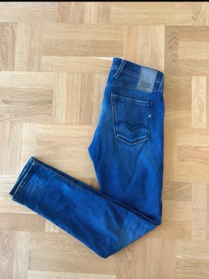 Blå slim fit jeans från Replay anbass hyperflex - Snygga blå slim fit jeans från Replay med klassisk femficksdesign och diskreta slitningar framtill. Jeansen har normal midja och raka ben. Tillverkade i mjukt denimtyg som ger en bekväm känsla och passar perfekt till en avslappnad stil. Model, anbass hyperflex.