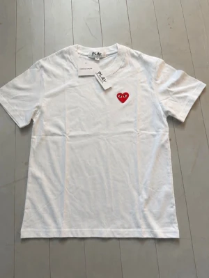 Vit t-shirt Comme des Garçons Play - Vit t-shirt från Comme des Garçons Play med det ikoniska röda hjärtat med ögon broderat på bröstet. Klassisk rund hals och korta ärmar. Tillverkad i mjuk bomull för en skön och stilren look.