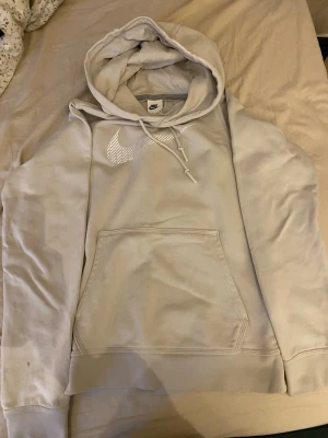 Beige hoodie från Nike med logga - Snygg beige hoodie från Nike med stor vit logga på bröstet. Klassisk känguruficka framtill och justerbar huva med dragsko. Perfekt för en avslappnad och sportig stil. Mjuk bomullsblandning som känns skön mot huden.