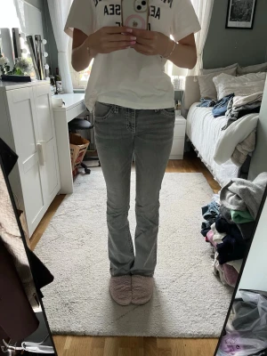 Gråa bootcut jeans med kontrastsömmar - Säljer ett par gråa bootcut jeans med snygga kontrastsömmar och detaljerade bakfickor. Jeansen har normal midja och klassisk femficksdesign. Perfekta för dig som vill ha en avslappnad men ändå trendig look.