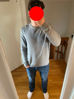 Ljusgrå basic stickad tröja - En stilren ljusgrå stickad tröja med rund halsringning och ribbade muddar vid ärmslut och nederkant. Perfekt för lager på lager och enkel att matcha med olika outfits. Tröjan har en klassisk passform och är tillverkad i mjukt material.