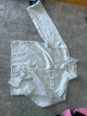 Ljus zebramönstrad skjorta Gina Tricot - Ljus pyjamas skjorta från Gina Tricot med subtilt zebramönster i vitt och ljusgrått. Skjortan har klassisk krage, knappstängning och en bröstficka. Perfekt för dig som gillar mjuka material och stilrena detaljer.