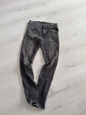 Grå slim fit jeans från Replay - Snygga grå slim fit jeans från Replay med klassisk femficksmodell och diskreta slitningar. Jeansen har normal midja och dragkedjegylf. Perfekta för dig som gillar en avslappnad men ändå stilren look.