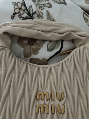 Beige handväska från Miu Miu - Säljer en beige handväska från Miu Miu i mjukt, quiltat läder med guldfärgade detaljer och logotyp framtill. 