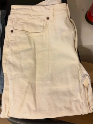 Klassiska vita raka jeans - Säljer ett par vita jeans med rak passform och fem fickor. Jeansen har en tidlös look med metallknappar och nitar. Tillverkade i ett kraftigare bomullstyg som ger en snygg och clean stil. Perfekta att matcha med allt i garderoben.
