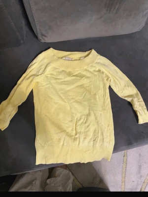 Gul stickad tröja med rund hals - Ljusgul stickad tröja med rund halsringning och ribbade muddar vid ärmslut och nederkant. Tröjan har en enkel och stilren design, perfekt att matcha med jeans eller kjol. Långärmad och mjuk i materialet.