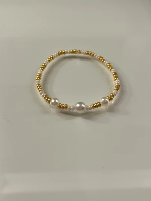 Pärlarmband med guldiga detaljer - Snyggt armband med vita och guldiga pärlor i olika storlekar. Armbandet har en elastisk tråd som gör det enkelt att ta på och av. Perfekt accessoar för att lyfta din stil med en elegant touch.