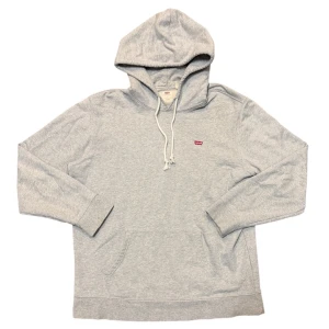 Levi's Small Logo Grey Hoodie - Den här varan kommer auktioneras ut på Sneakershyllan x Plick Live Torsdagen 10 september kl 19 med ett startpris på endast 10 kr. Ljusgrå klassisk hoodie från Levi's med liten logga. Vita snören, något fransiga. Fläck på ena armmudden 