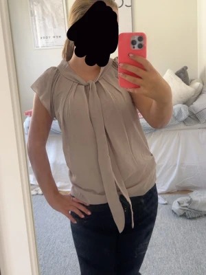 Beige blus med knytband i halsen - Snygg beige blus med knytband i halsen och korta ärmar. Köpt secondhand men har knappast använt den, kom gärna med prisförslag eller frågor!💕