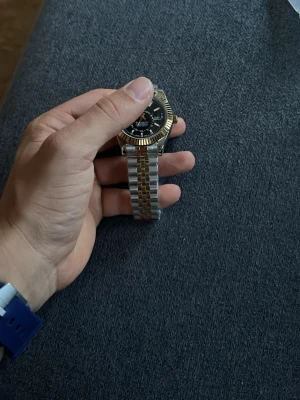 Stilren klocka i guld och silver - Säljer en snygg klocka med tvåfärgad länk i guld och silver. Urtavlan är svart med tydliga markeringar och boetten har en guldfärgad kant. Perfekt accessoar för att lyfta din outfit.