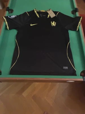 Svart Nike fotbollströja Palmer 10 - Snygg Chelsea fotbollströja i svart med gula detaljer. Palmer #10 på ryggen, Chelsea-emblem och Nike-logga framtill samt Premier League-detaljer på ärmen.  Storlek: L Skick: Ny med tags Färg: Svart med gula detaljer Material: Polyester Spelare: Cole Palmer #10