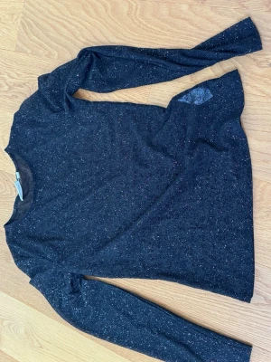 Svart glittrig topp från Kappahl - Svart långärmad topp från Kappahl med glittriga detaljer. Tunn och stretchig modell som sitter snyggt på kroppen. Perfekt för dig som vill ha lite extra glitter i vardagen.