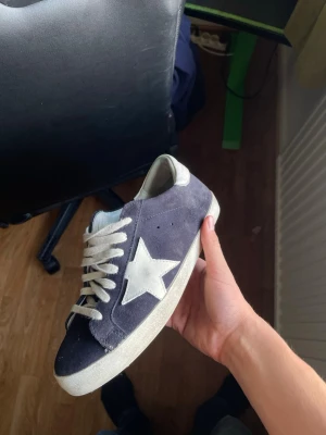 Mörkblå sneakers med vit stjärna - Snygga mörkblå sneakers i mocka med vit stjärndetalj på sidan och vita skosnören. Skon har en vit sula och en låg profil som ger en klassisk streetwear-look. Perfekt för dig som gillar stilrena och trendiga sneakers.