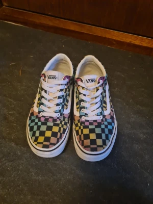 Vans skor - Färgglada Vans sneakers med klassiskt checkerboard-mönster i blått, gult, rosa och svart. Skorna har vit sula, vita skosnören och den ikoniska vita sidostripen. Använda ett fåtal gånger. Är i mycket bra skick.