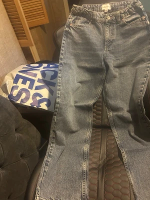 Blå raka jeans med hög midja - Säljer ett par blå jeans med rak passform och hög midja. Jeansen har klassisk femficksdesign och är tillverkade i denim. Perfekta för en avslappnad och trendig look.