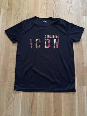 Svart Dsquared2 ICON t-shirt - Svart t-shirt från Dsquared2 med färgglad 'ICON'-text på bröstet och diskret logga ovanför. Tillverkad i 100% polyester med klassisk rund hals och korta ärmar. Perfekt för dig som vill sticka ut med en ikonisk look.