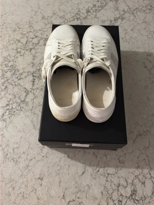 Vita låga sneakers i läder - Stilrena vita sneakers med lågt skaft och klassisk snörning. Ovandelen är i slätt läder med perforerade detaljer på sidorna för extra ventilation. Sulan är vit med en något offwhite nyans. Perfekta för en clean och enkel look.