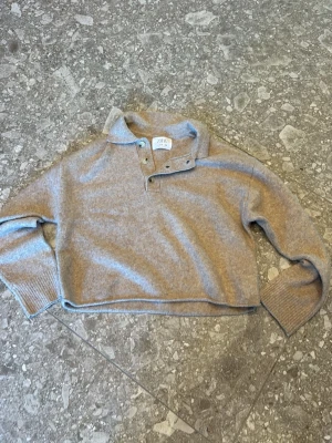Beige stickad tröja från Zara - Säljer en beige stickad tröja från Zara med krage och knappslå framtill. Tröjan har långa ärmar och ribbade muddar vid ärmslut och nederkant. Perfekt för en avslappnad och stilren look.