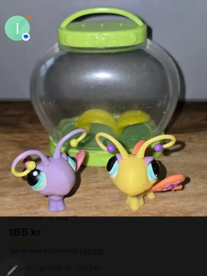 Littlest Pet Shop ,Hasbro 2005 - Två färgglada Littlest Pet Shop figurer, en lila och en gul med stora ögon och antenner. Medföljer ett genomskinligt plastakvarium med grönt lock och handtag samt dekorationer inuti. Perfekt för samlare eller som leksak.