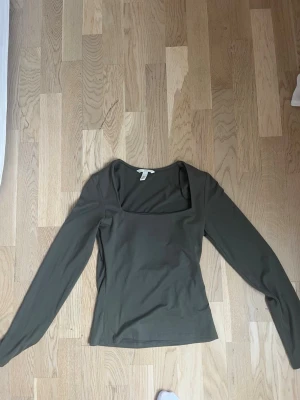 Olivgrön långärmad topp från H&M - Snygg olivgrön långärmad topp från H&M med fyrkantig ringning. Tillverkad i mjukt och stretchigt material som sitter bekvämt och har en slim passform. Perfekt att styla med jeans eller kjol för en trendig look.