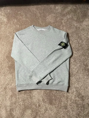 Stone island tröja - Grå Stone Island sweatshirt med klassisk, stilren design. Försedd med Stone Island-badge på ärmen och ribbade muddar vid ärmslut, hals och nederkant. Enkel att matcha och passar både till jeans och mjukisbyxor.  📏 Storlek: S 🎨 Färg: Grå ✨ Skick: Mycket bra skick