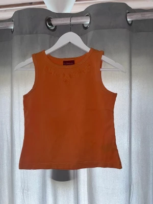 Orange broderad linnetopp från L.O.G.G. - Snygg orange linnetopp från L.O.G.G. med broderade blommor vid halsringningen. Toppen är ärmlös och har en enkel, rak passform. Perfekt för varma dagar och enkel att matcha med jeans eller kjol.