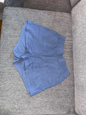 Blå linneshorts från 157 - Säljer ett par ljusblå shorts från 157 i luftig linnemix. De har elastisk midja och avslappnad passform, perfekta för varma dagar. Shortsen har fickor på sidorna och enkel, stilren design.