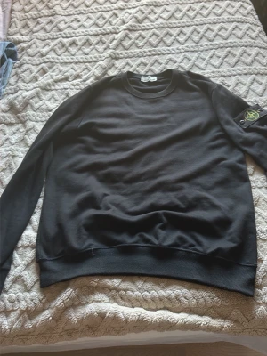 Svart sweatshirt från Stone Island - Säljer en svart sweatshirt från Stone Island med den klassiska logotypen på vänster ärm. Tröjan har rund halsringning, ribbade muddar och är tillverkad i mjukt bomullsmaterial. Perfekt för en avslappnad och stilren look. Lappen är helt paj, hände under tiden min lillebrorsa var extremt sur på mig så gissar att han har gjort nått.