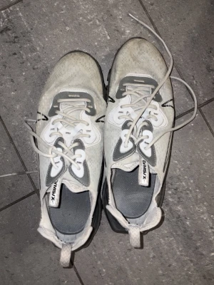 Nike React Element 55 vita sneakers - Nike React Element 55 sneakers i vitt och grått med svarta detaljer. Skorna har en sportig design, mesh-överdel och synlig Nike-logga på sidan. Sulan är tjock och ger bra dämpning. Perfekta för dig som gillar streetwear och en clean look.