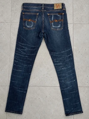 Nudie Jeans 29/34 - Säljer ett par blå smala jeans från Nudie Jeans med slitningar och whiskers på både fram- och baksida. Jeansen har klassiska fem fickor, kontrastsömmar och Nudie-logga på bakfickan. Tillverkade i denim med en snygg tvättad look.