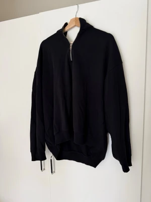 Svart hoodie med halv dragkedja Weekday - Säljer en svart hoodie från Weekday med halv dragkedja framtill och huva. Oversized passform och långa ärmar. Tillverkad i mjukt bomullsmaterial som känns skönt mot huden. Perfekt för en avslappnad och stilren look. Bra skick. Storlek M